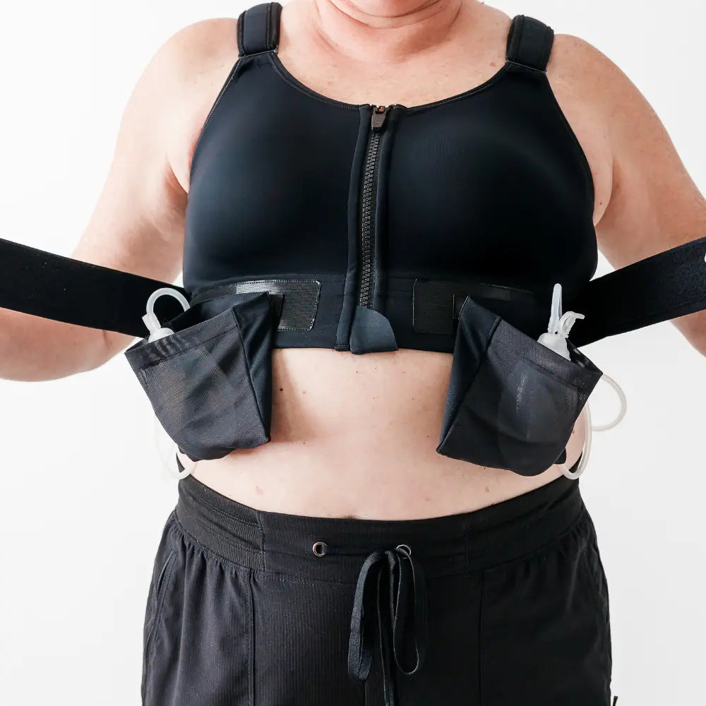 A woman wearing a black Resilience Bra with attached yet removable drain bags on a white background
