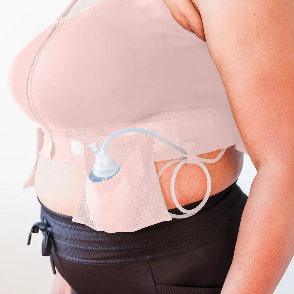 A woman wearing her resilience bra in the shade pink while showing the removable drain pockets that hold up to 3 bulbs per side